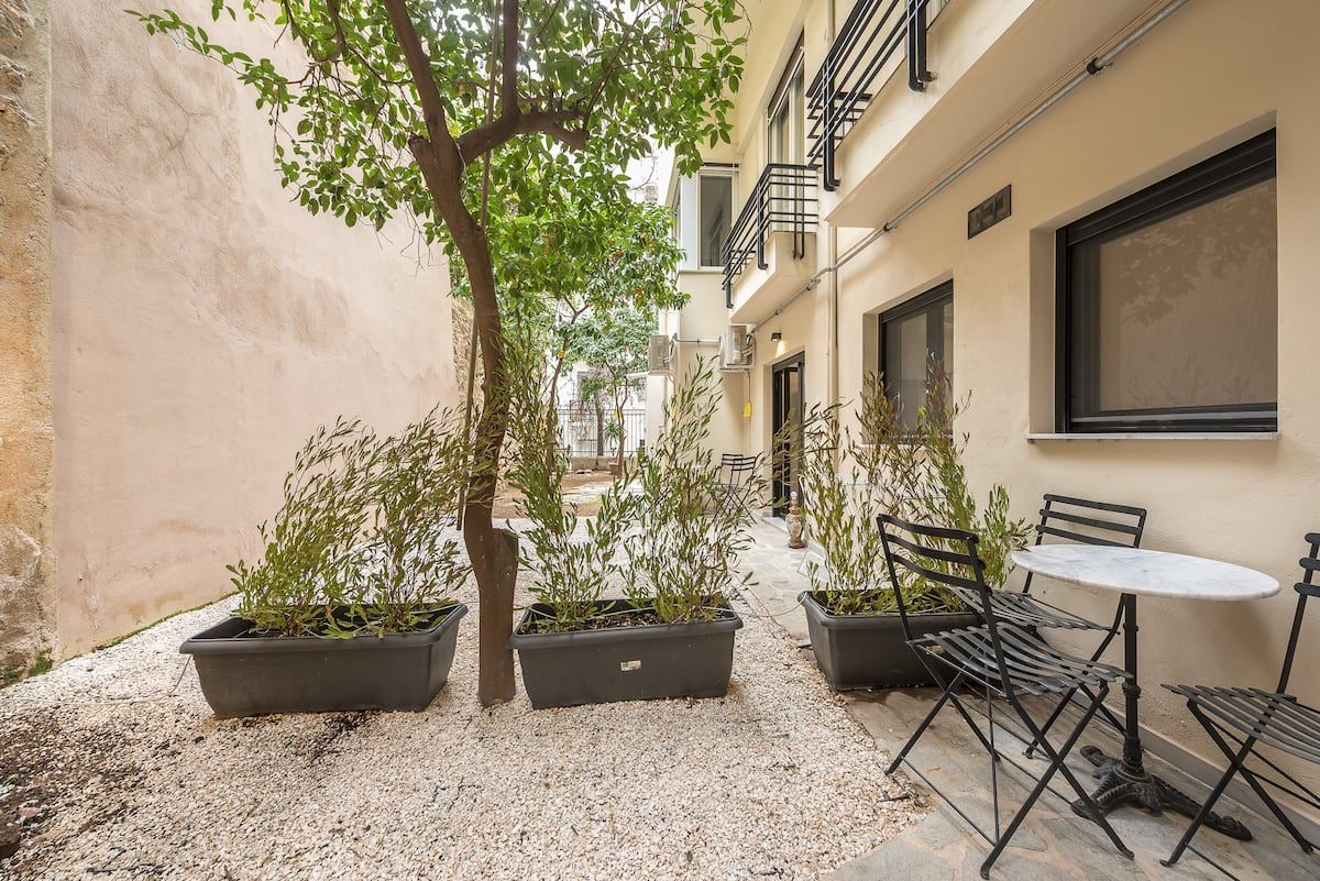 The private courtyard: a citrus tree, gravel, planters and a bistro table beside the apartment's windows.